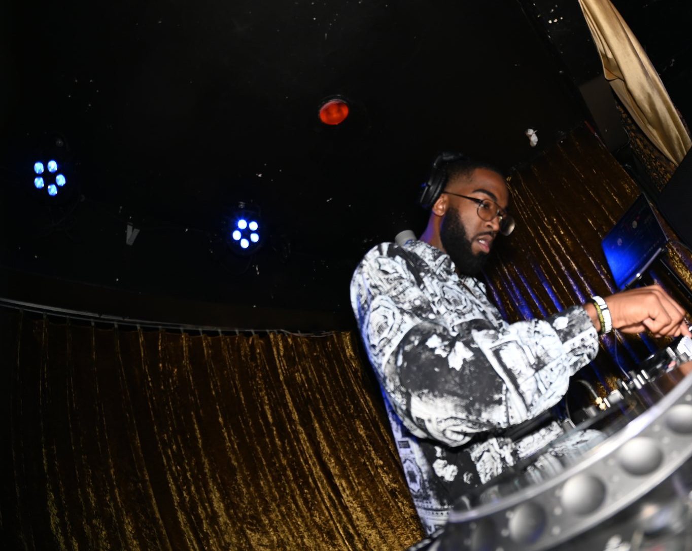 A club room, gold curtain and stage lights, the decks at the right edge